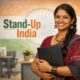 Confident Indian woman entrepreneur holding a folder in a modern office with Stand-Up India text and Indian flag backdrop.